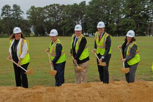 Five people standing in front of a mound of dirt with shovels signifying breaking ground for the new hospital for the chronically ill.